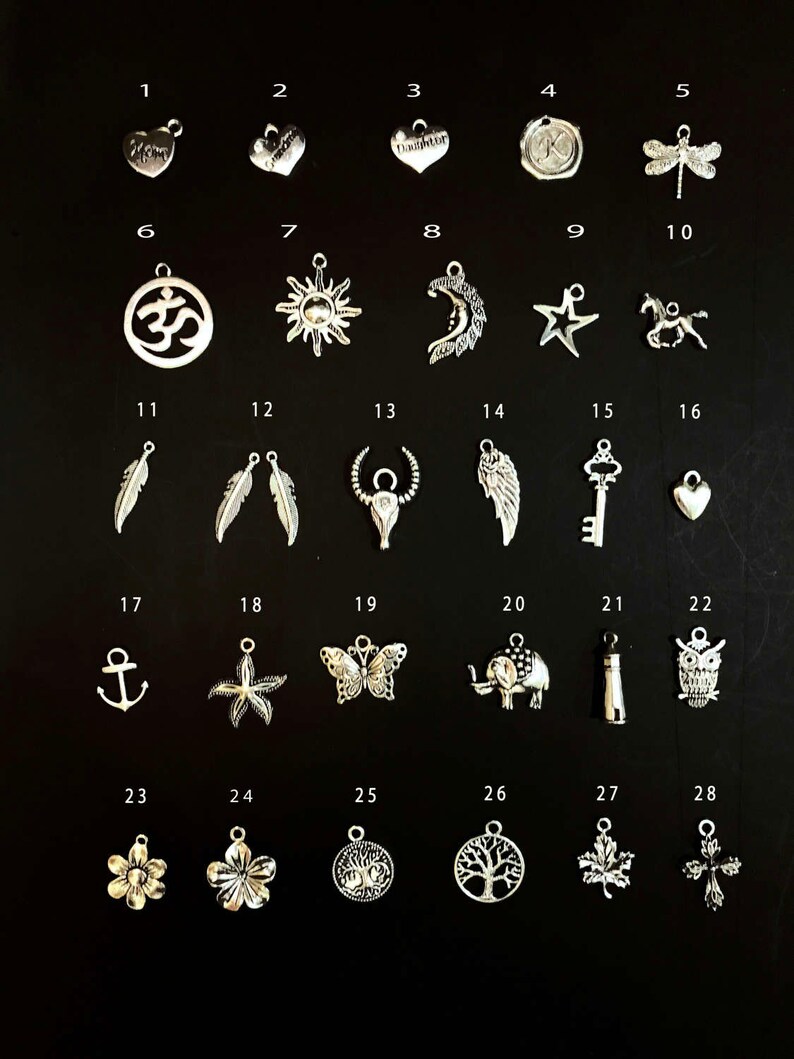 May include: A set of 28 silver charm pendants with various designs, including hearts, stars, animals, and symbols. The charms are arranged in rows on a black background.