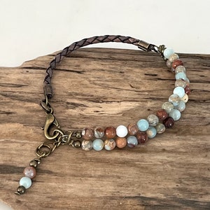 May include: A brown leather bracelet with a double row of beads. The beads are a mix of light blue, brown, and white. The bracelet has a brass clasp.