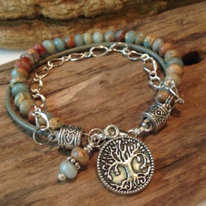 May include: A double-strand bracelet with a silver chain and a tree of life charm. The bracelet is made with light blue and brown stones.