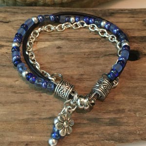 May include: A layered bracelet with blue and silver beads, a silver chain, and a silver flower charm.
