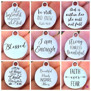 May include: Nine silver charm pendants with inspirational quotes and phrases. The charms are round and have a hole at the top for attaching to a chain or bracelet. The quotes include "She believed she could so she did", "Be still and know", "God is within her she will not fall", "Blessed", "I am Enough", "Strong Fearless Beautiful", "I can do all things through Christ who strengthens me", "Beautiful Minds Inspire Others", and "Faith over Fear".