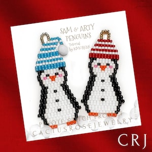 May include: Two beaded penguin ornaments with red and blue striped hats. The ornaments are labeled "Sam & Arty Penguins" and "Cactus Rose Jewelry".
