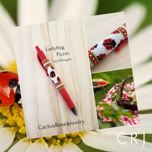 May include: A red pen with a white and black beaded ladybug design. The pen is on a wooden surface with the text "Ladybug Picnic by K.Morgan" and "CactusRoseJewelry".