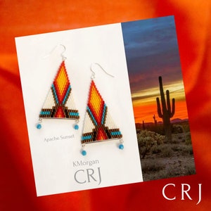 Può includere: Un paio di orecchini con perline con un design geometrico in tonalità di bianco, arancione, giallo, marrone e turchese. Gli orecchini sono etichettati "Apache Sunset" e "KMorgan CRJ".