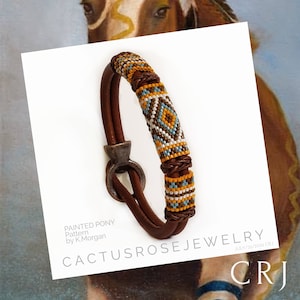 May include: A brown leather bracelet with a beaded design in shades of brown, yellow, white, and blue. The bracelet has a silver clasp and is labeled "Painted Pony Pattern by K. Morgan" and "Cactusrose Jewelry".