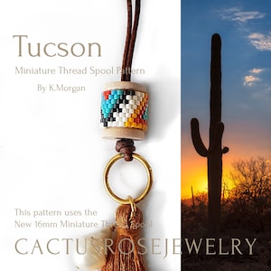 May include: A beaded thread spool necklace with a brown leather cord, a gold ring, and a brown tassel. The spool is decorated with colourful beads in a geometric pattern. The background is a sunset with a silhouette of a cactus.