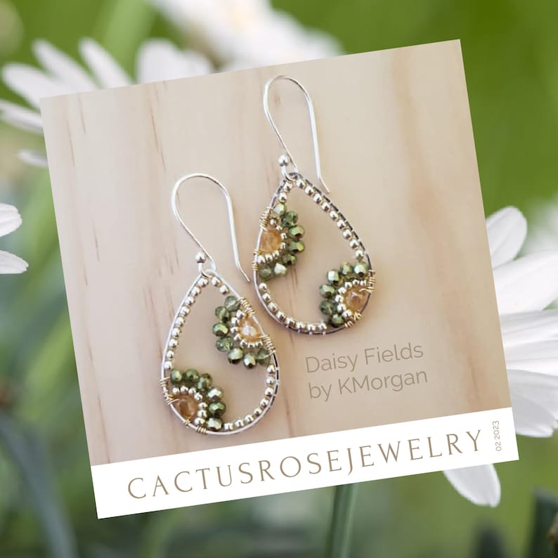 May include: A pair of teardrop-shaped earrings with a silver wire frame and green and gold beads. The earrings are displayed on a wooden surface with the text "Daisy Fields by KMorgan" and "Cactusrosejewelry" visible.