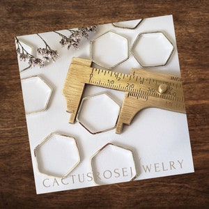 May include: A set of six silver hexagon-shaped metal rings, measured with a ruler in inches. The rings are on a white surface with the text "Cactus Rosej Welry" in the bottom right corner.