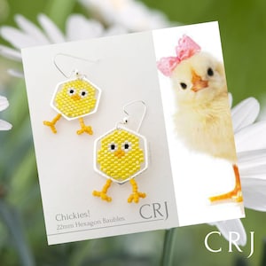 Peut inclure: Une paire de boucles d'oreilles en argent avec des motifs de poussins jaunes. Les boucles d'oreilles sont faites avec des boules hexagonales de 22 mm. Les boucles d'oreilles sont présentées sur un fond blanc avec un poussin jaune en arrière-plan. Le texte "Chickies! 22mm Hexagon Baubles" et "CRJ" sont également affichés sur l'image.