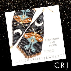 Peut inclure: Une paire de longues boucles d'oreilles noires en perles avec un motif de papillon bleu et orange et des croissants de lune blancs. Les boucles d'oreilles sont étiquetées "Luna Moth and Moon" et "Cactusrosejewelry CRJ 2.25.2022".