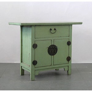 May include: A small, green wooden cabinet with two doors and a drawer. The cabinet has decorative metal accents and sits on four legs.