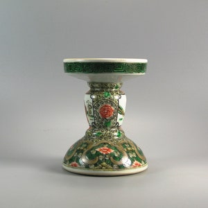 Pode incluir: Um casti&ccedil;al decorativo de cer&acirc;mica com base branca e borda verde. O casti&ccedil;al apresenta um design floral com flores vermelhas e laranjas e detalhes verdes e dourados. A parte superior tem um padr&atilde;o geom&eacute;trico verde.
