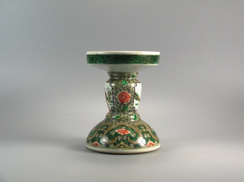 Pode incluir: Um casti&ccedil;al decorativo de cer&acirc;mica com base branca e borda verde. O casti&ccedil;al apresenta um design floral com flores vermelhas e laranjas e detalhes verdes e dourados. A parte superior tem um padr&atilde;o geom&eacute;trico verde.