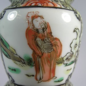 Pode incluir: Vaso de cer&acirc;mica branca com um design detalhado pintado &agrave; m&atilde;o. O vaso apresenta uma figura em vestes vermelhas, com paisagens e detalhes florais em verde, laranja e preto. O vaso tem uma forma bulbosa.