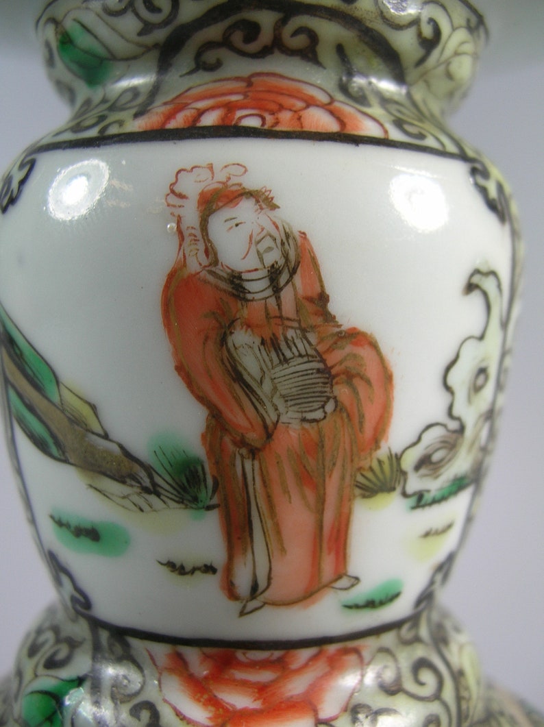 Pode incluir: Vaso de cer&acirc;mica branca com um design detalhado pintado &agrave; m&atilde;o. O vaso apresenta uma figura em vestes vermelhas, com paisagens e detalhes florais em verde, laranja e preto. O vaso tem uma forma bulbosa.