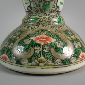 Pode incluir: Close-up de um objeto decorativo de cer&acirc;mica. A base apresenta um design floral com detalhes em laranja, verde e dourado. O objeto tem uma base branca e uma forma bulbosa, com padr&otilde;es pintados intrincados.