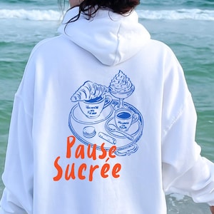 May include: White hoodie with a blue and orange graphic on the back. The graphic features a croissant, coffee, and the words "Pause Sucrée". The word "White" is printed at the bottom right.