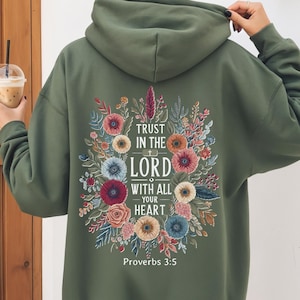 May include: Military green hoodie with floral design and the text "Trust in the Lord with all your heart" and "Proverbs 3:5". The hoodie has a drawstring hood and long sleeves.