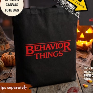 May include: A black cotton tote bag featuring the red text BEHAVIOR THINGS printed on the front. The bag measures 15 inches by 16 inches. A smaller inset image shows the back of the bag with the same red text printed in a smaller size.