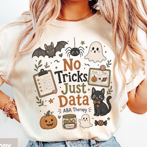 May include: An ivory t-shirt featuring a Halloween-themed graphic with the text "No Tricks, Just Data" and "ABA Therapy". The design includes a bat, spider, ghosts, a clipboard, a pumpkin, a token jar, a black cat, and a "First/Then" visual schedule.