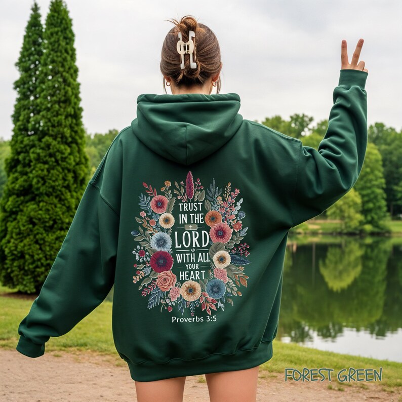 Puede incluir: Sudadera con capucha verde bosque con un dise&ntilde;o floral y el texto "Trust in the Lord with all your heart" y "Proverbios 3:5". La sudadera tiene una capucha con cord&oacute;n y un bolsillo de canguro.