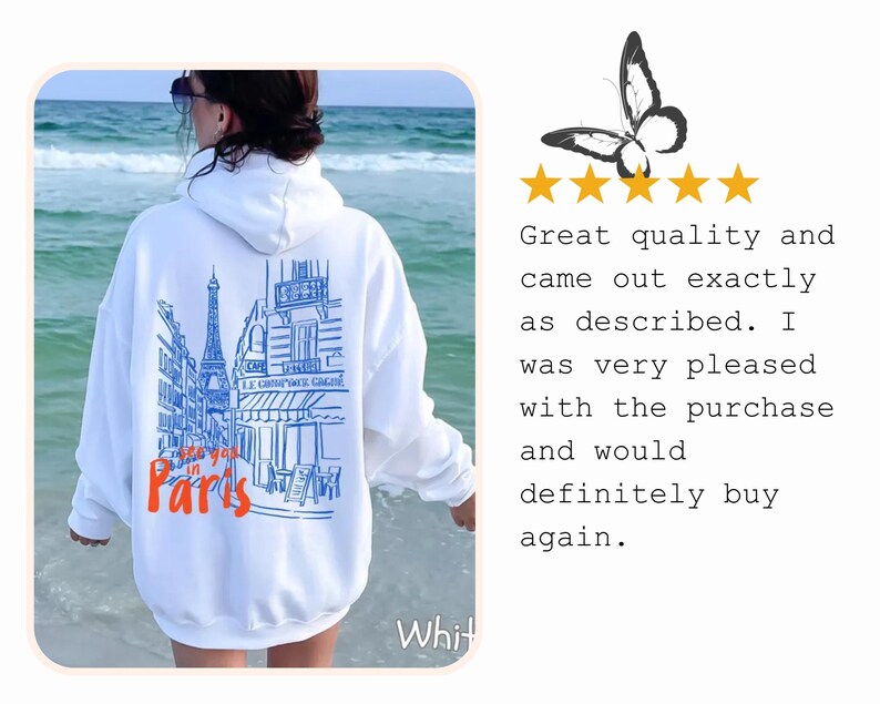 May include: A white hooded sweatshirt featuring a blue line-art illustration of a Parisian street scene with the Eiffel Tower and the text "see you in Paris" in orange. The back of the garment displays this graphic design clearly.