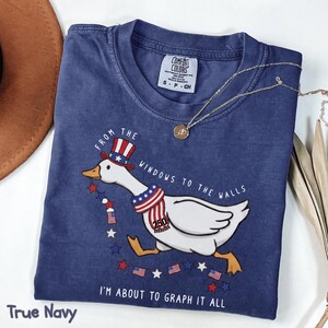 May include: A navy blue t-shirt with a graphic of a goose wearing a patriotic hat and scarf, with the text "FROM THE WINDOWS TO THE WALLS" and "I'M ABOUT TO GRAPH IT ALL". The shirt is labeled "True Navy".