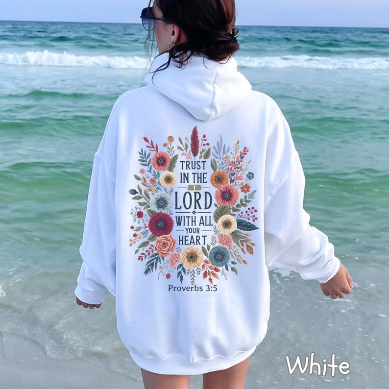 Puede incluir: Sudadera con capucha blanca con un dise&ntilde;o floral y el texto "Trust in the Lord with all your heart" de Proverbios 3:5. El dise&ntilde;o presenta flores coloridas en tonos rojos, naranjas y azules.