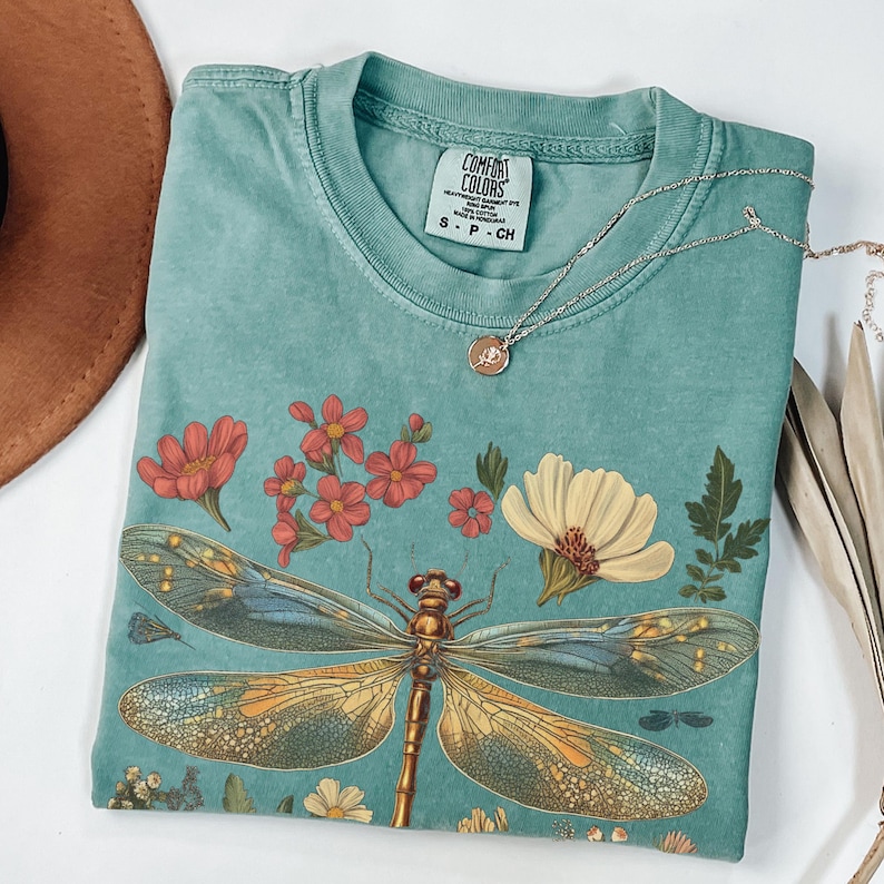 This Women's Dragonfly Floral T-Shirt is a vintange-inspired, nature-inspired tee that is perfect for garden lovers and those who embrace the cottagecore aesthetic. It exudes a peaceful and whimsical vibe, making it a great addition to a nature lover's wardrobe. Ideal for casual wear or as a thoughtful gift for a loved one who enjoys botanical designs. Relevant for Earth Day, birthdays, and any nature-themed celebrations.