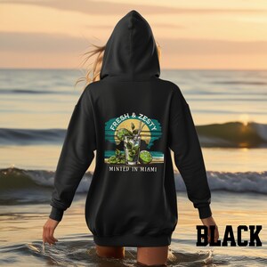 Turn up the tropical energy with our Fresh & Zesty – Minted in Miami hoodie, featuring a bold mojito graphic set against a dreamy Miami sunset beach scene. This eye-catching back print channels sunny coastal vibes, citrusy freshness, and laid-back luxury—perfect for sipping mojitos or dreaming of South Beach. A go-to for travel, lounging, or gifting anyone who loves cocktails, sunshine, and Miami heat.  Ideal gift for cocktail lovers, beachgoers, or anyone with a thing for Miami vibes.