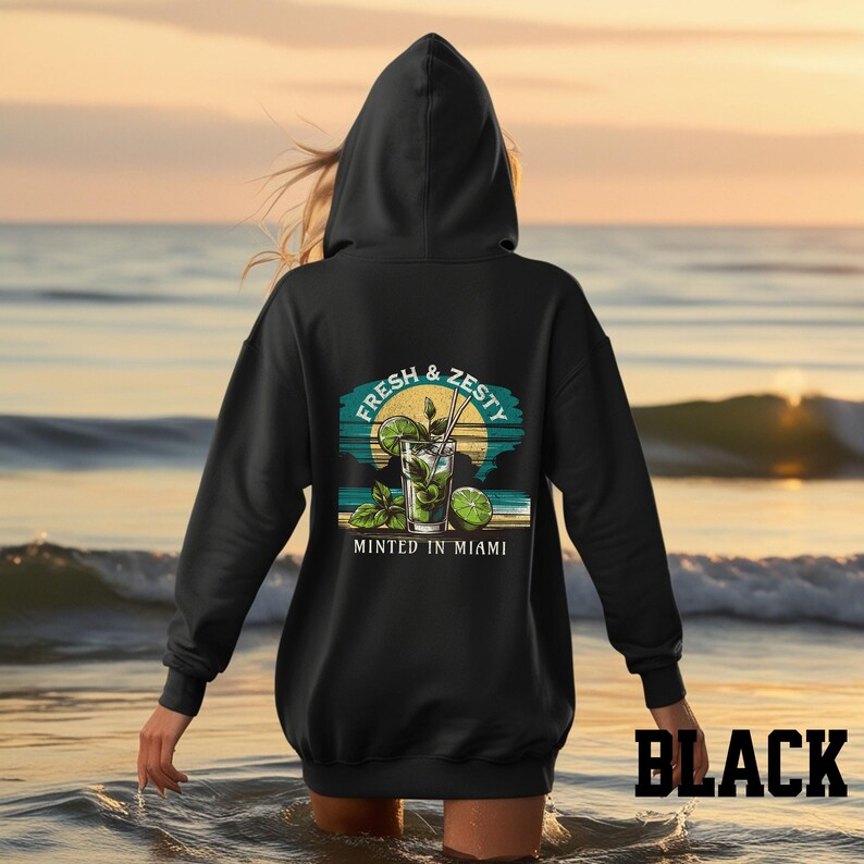Turn up the tropical energy with our Fresh & Zesty – Minted in Miami hoodie, featuring a bold mojito graphic set against a dreamy Miami sunset beach scene. This eye-catching back print channels sunny coastal vibes, citrusy freshness, and laid-back luxury—perfect for sipping mojitos or dreaming of South Beach. A go-to for travel, lounging, or gifting anyone who loves cocktails, sunshine, and Miami heat.  Ideal gift for cocktail lovers, beachgoers, or anyone with a thing for Miami vibes.