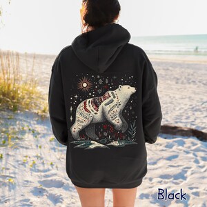 May include: Black hoodie with a detailed illustration of a polar bear adorned with intricate patterns. The design includes a starry sky, sun, and floral elements. The word "Black" is printed at the bottom of the hoodie.