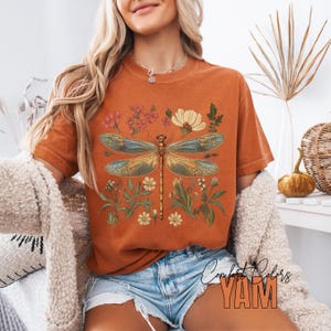 This Women's Dragonfly Floral T-Shirt is a boho and nature-inspired tee that is perfect for garden lovers and those who embrace the cottagecore aesthetic. It exudes a peaceful and whimsical vibe, making it a great addition to a nature lover's wardrobe. Ideal for casual wear or as a thoughtful gift for a loved one who enjoys botanical designs. Relevant for Earth Day, birthdays, and any nature-themed celebrations.