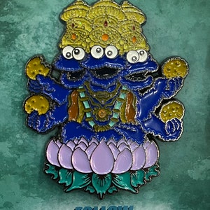 May include: A blue Cookie Monster pin with multiple eyes, wearing a gold crown and sitting on a purple lotus flower. The pin is holding cookies in each hand.