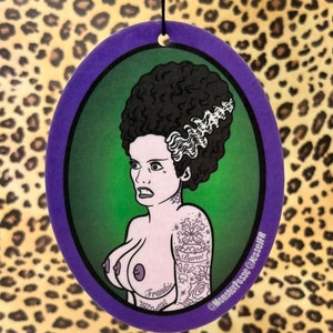 May include: A purple and green round car air freshener with a cartoon image of a woman with green hair and a tattoo that says "Burrat" on her arm. The text "Frankie" is below the image and the text "@MonsterPose @JesseJFR" is on the bottom right corner.