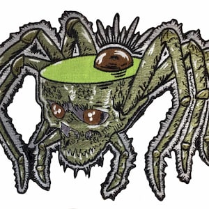 Peut inclure: Un patch brodé représentant une araignée avec un crâne pour tête. L'araignée est verte et grise, avec huit pattes et un grand œil rond.