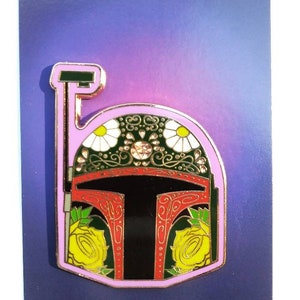 Op de afbeelding: Een zwarte en rode emaille pin met een gouden rand, met een gestileerde Boba Fett helm met bloemmotieven. De helm is versierd met gele rozen, witte madeliefjes en groene bladeren. De pin is op een paarse en blauwe achtergrond met de tekst "Jesse JFR" onderaan.