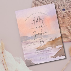 Può includere: Un invito di nozze ad acquerello con uno sfondo di tramonto rosa, viola e arancione. L'invito recita "Sei invitato al matrimonio di Ashley e Jackson, sabato 16 maggio 2026, alle 17:00, Switzer Farm, 56700 North Highway 1, Westport, CA 95485."