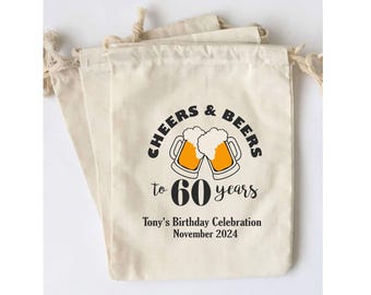 Puede incluir: Una bolsa de algodón blanco con cordón de ajuste con el texto "Cheers & Beers to 60 years" y un gráfico de dos jarras de cerveza con espuma. La bolsa también incluye el texto "Tony's Birthday Celebration November 2024".