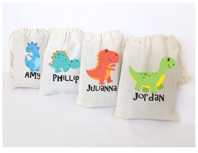 Puede incluir: Cuatro peque&ntilde;as bolsas de lona blanca con cierre de cord&oacute;n. Cada bolsa presenta un dise&ntilde;o de dinosaurio diferente y un nombre impreso debajo: Amy, Phillip, Julianna y Jordan.