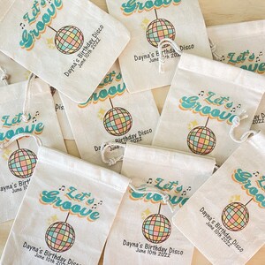 May include: A set of nine white fabric drawstring bags with a retro 70s design. The bags feature a colorful disco ball, the text "Let's Groove", and the words "Dayna's Birthday Disco" with the date "June 10th 2022".