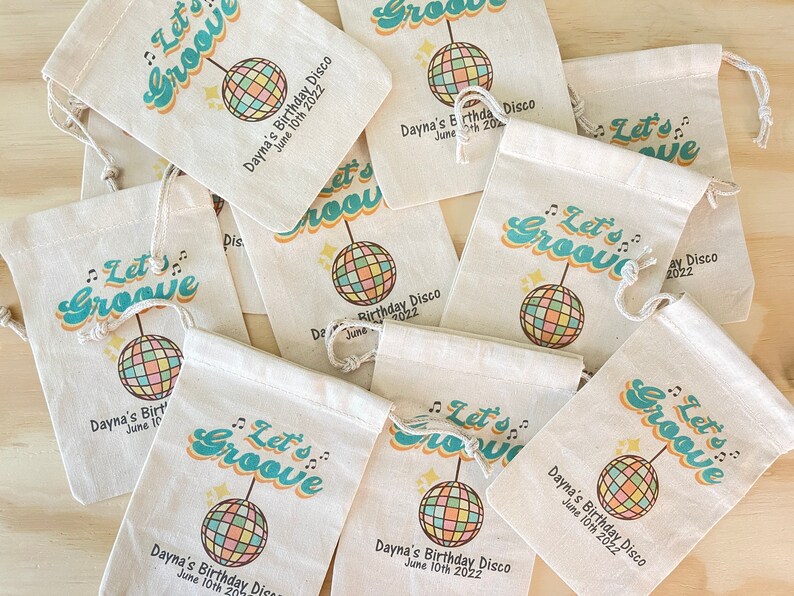 May include: A set of nine white fabric drawstring bags with a retro 70s design. The bags feature a colorful disco ball, the text "Let's Groove", and the words "Dayna's Birthday Disco" with the date "June 10th 2022".