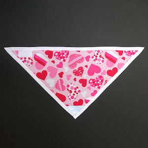 May include: A pink and white fabric bandana with a heart pattern. The bandana is triangular in shape and has a white border.