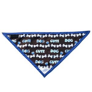 May include: A brown dog bandana with a blue border. The bandana has a repeating pattern of white bones, blue paw prints, and the words "DOG CUTE" in blue.