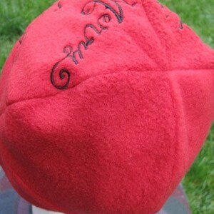 May include: Red fleece beanie with black embroidered text that reads "Embrace the Air".
