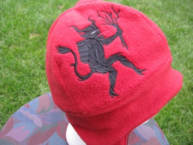 May include: Red fleece hat with a black embroidered devil holding a branch.