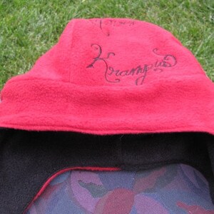 May include: Red fleece hat with a black fleece lining and the word "Krampus" embroidered in black on the front.