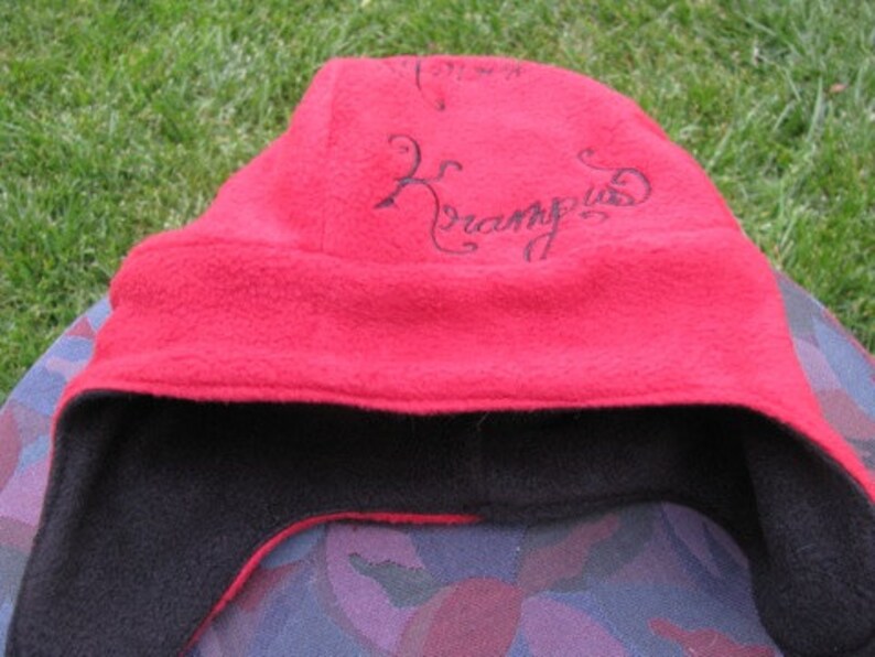 May include: Red fleece hat with a black fleece lining and the word "Krampus" embroidered in black on the front.