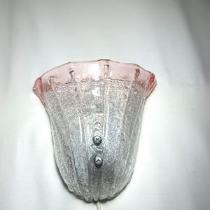 May include: A vintage wall sconce with a frosted glass shade and a pink rim. The shade has a textured, rippled surface and is attached to a metal base with two screws.