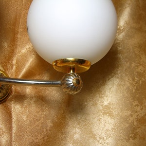 May include: A silver and gold wall sconce with two white glass globes. The sconce has a curved arm and decorative details.